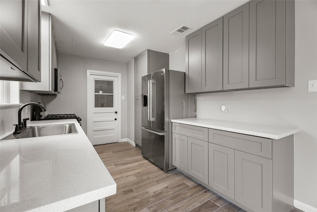 kitchen with gray cabinets, a sink, stainless steel appliances, light wood finished floors, and light countertops