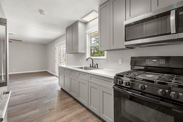 kitchen featuring black gas range oven, stainless steel microwave, gray cabinetry, a sink, and light countertops