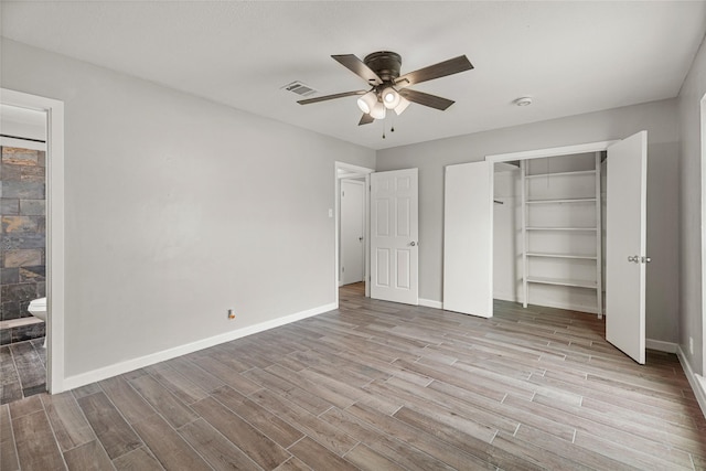 unfurnished bedroom with wood finished floors, baseboards, a closet, and ensuite bath