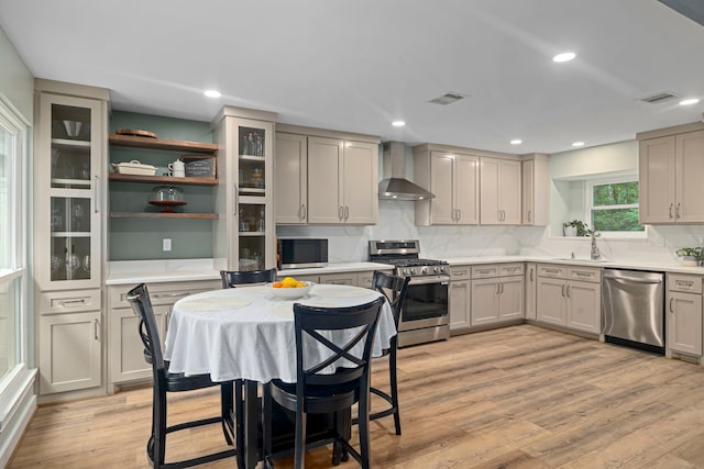13 Leverwood Ct, The Woodlands, TX 77381 - kitchen with stainless steel appliances, wall chimney exhaust hood, a sink, light wood-style flooring, and light countertops