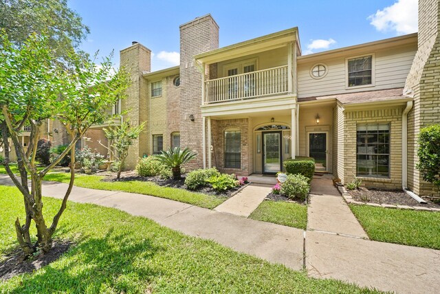 view of property featuring a balcony, brick siding, a chimney, and a front lawn