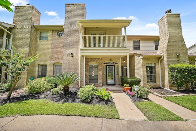 view of front of property with a balcony, a chimney, and brick siding