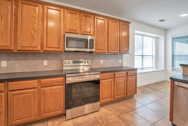 12139 Canyon Arbor Way, Houston, TX 77095 - kitchen with appliances with stainless steel finishes, dark countertops, brown cabinetry, tasteful backsplash, and light tile patterned floors
