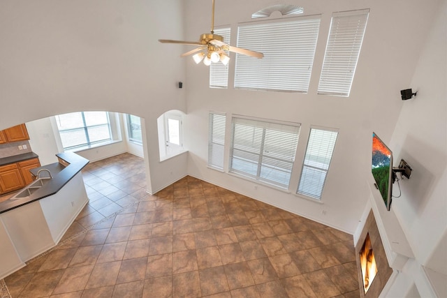 12139 Canyon Arbor Way, Houston, TX 77095 - unfurnished living room featuring a high ceiling, a ceiling fan, arched walkways, a lit fireplace, and a sink