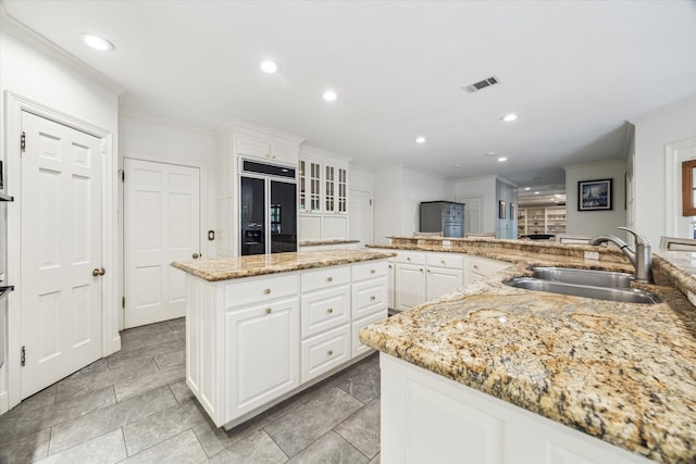 kitchen featuring paneled built in refrigerator, a sink, ornamental molding, a center island, and white cabinets