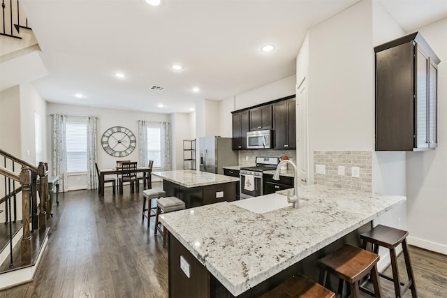 kitchen featuring appliances with stainless steel finishes, a center island, a kitchen breakfast bar, dark wood-type flooring, and backsplash