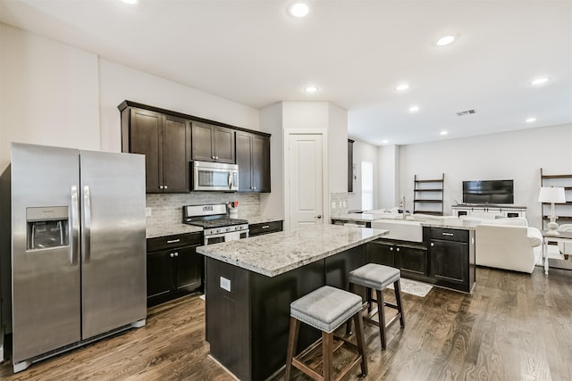 kitchen featuring appliances with stainless steel finishes, a center island, a sink, open floor plan, and dark wood-type flooring