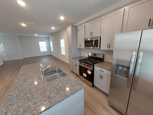 kitchen with appliances with stainless steel finishes, a sink, light wood-style flooring, decorative backsplash, and recessed lighting