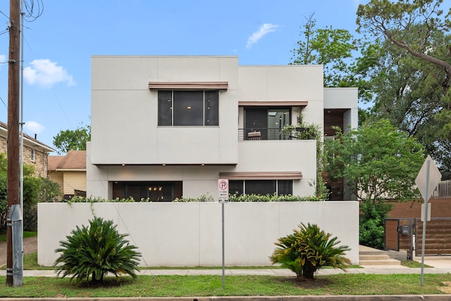contemporary home with a fenced front yard, stucco siding, and a balcony
