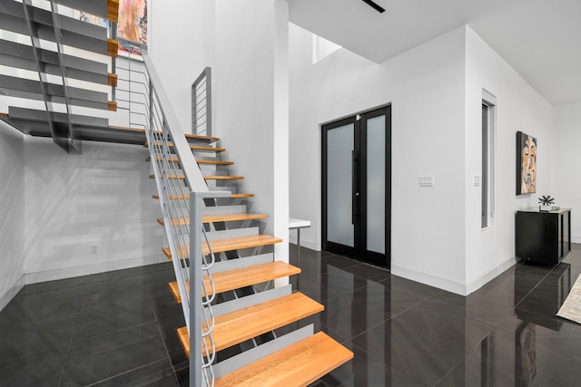 staircase with baseboards, granite tiled floors, and a high ceiling