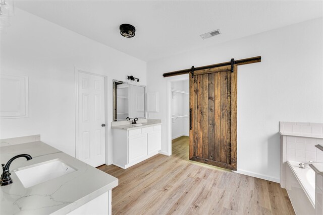 16219 Haden Crest Ct, Cypress, TX 77429 - bathroom featuring two vanities, wood finished floors, a garden tub, baseboards, and a closet