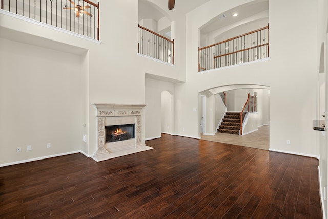 unfurnished living room featuring wood finished floors, a high end fireplace, a high ceiling, stairs, and baseboards