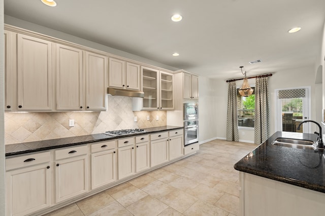kitchen featuring a sink, cream cabinets, under cabinet range hood, decorative backsplash, and appliances with stainless steel finishes