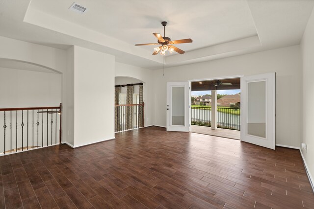 unfurnished room with a tray ceiling, a ceiling fan, baseboards, and wood finished floors