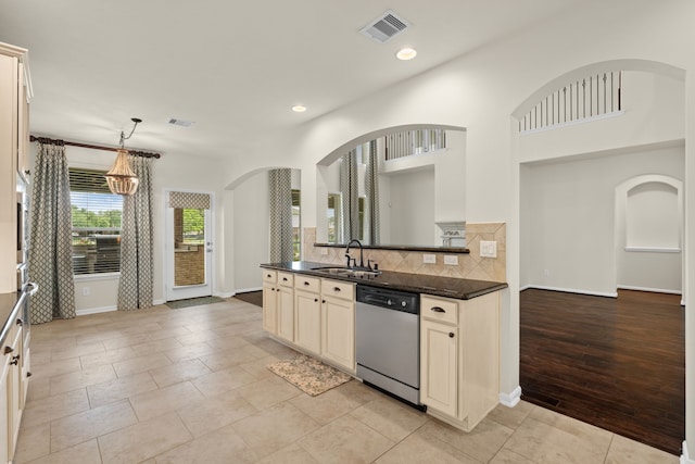 kitchen featuring dishwasher, a sink, dark countertops, arched walkways, and cream cabinetry