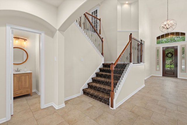 foyer entrance featuring a chandelier, stairway, a towering ceiling, baseboards, and light tile patterned floors