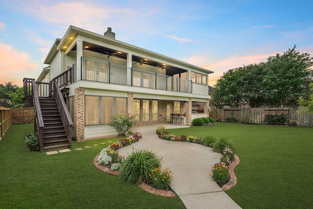 back of property at dusk with ceiling fan, a balcony, a patio, brick siding, and stairs