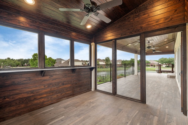 unfurnished sunroom featuring a ceiling fan, wood ceiling, a water view, lofted ceiling, and wood finished floors