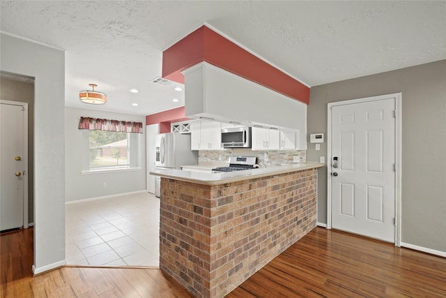 21410 Glenbranch Dr, Spring, TX 77388 - kitchen featuring appliances with stainless steel finishes, white cabinetry, light wood finished floors, light countertops, and a peninsula