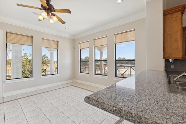 kitchen with healthy amount of natural light, light tile patterned floors, a ceiling fan, stone counters, and ornamental molding