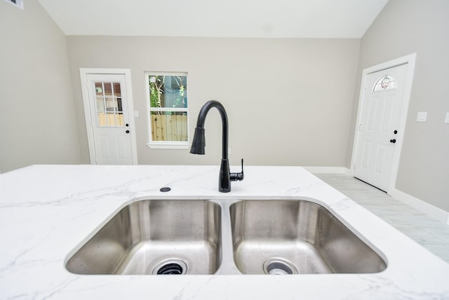 kitchen view of a sink, light stone countertops, and baseboards
