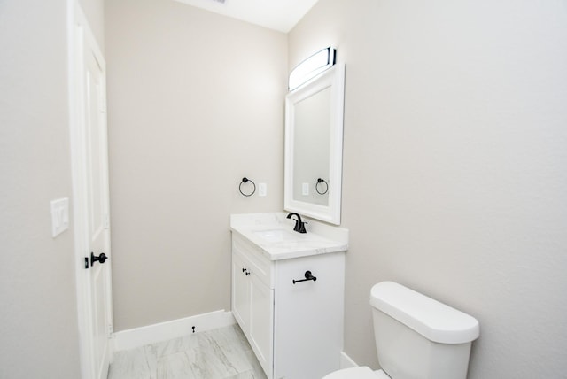 half bathroom featuring vanity, toilet, marble finish flooring, and baseboards
