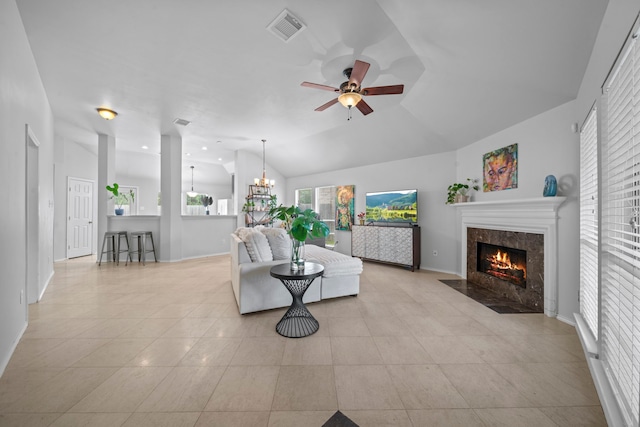 living area with ceiling fan, light tile patterned floors, a tiled fireplace, lofted ceiling, and a chandelier