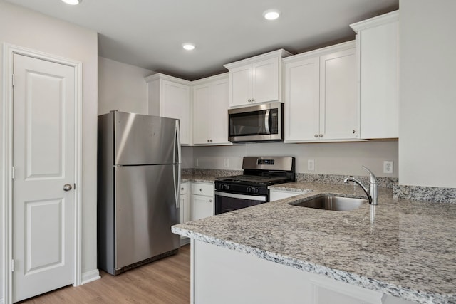 425 Tejas Trl, Waller, TX 77484 - kitchen with stainless steel appliances, a sink, white cabinetry, light stone countertops, and light wood finished floors