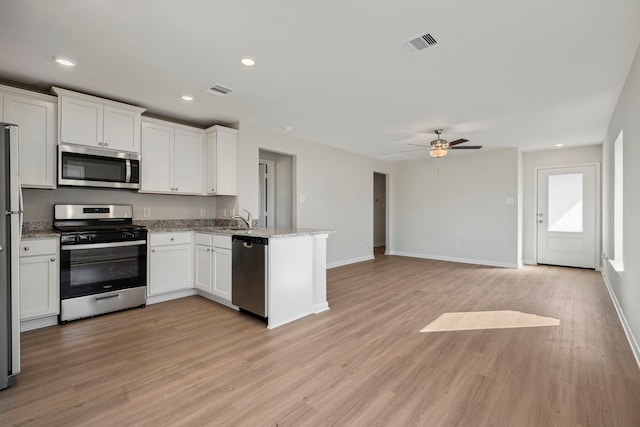 425 Tejas Trl, Waller, TX 77484 - kitchen with appliances with stainless steel finishes, a peninsula, light wood-style flooring, white cabinetry, and recessed lighting
