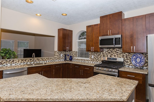kitchen with stainless steel appliances, a sink, light stone counters, a textured ceiling, and recessed lighting