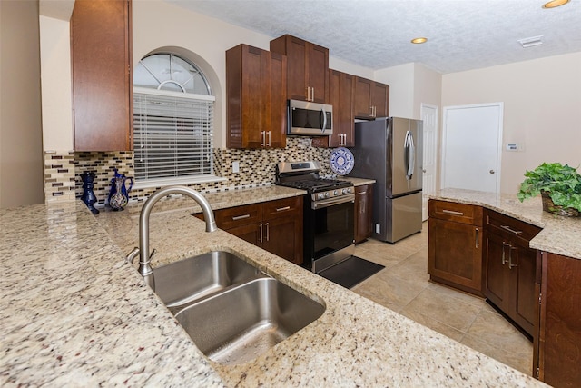 kitchen with appliances with stainless steel finishes, a sink, backsplash, light stone counters, and a textured ceiling