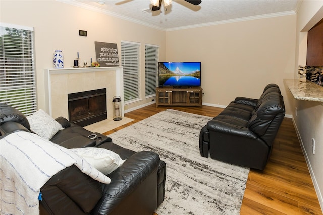 living area with a ceiling fan, a premium fireplace, wood finished floors, ornamental molding, and baseboards