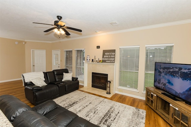 living area with a ceiling fan, wood finished floors, baseboards, crown molding, and a tiled fireplace
