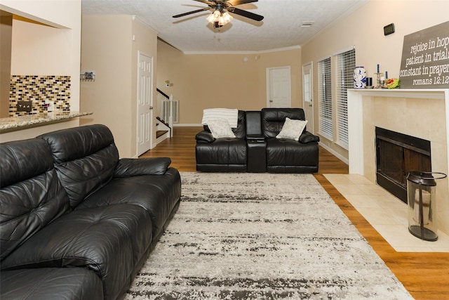 living area with a ceiling fan, wood finished floors, stairway, ornamental molding, and a tiled fireplace