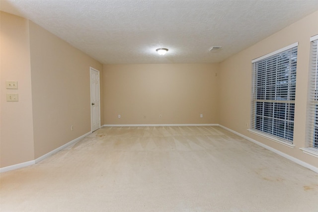 unfurnished room with light colored carpet, baseboards, and a textured ceiling