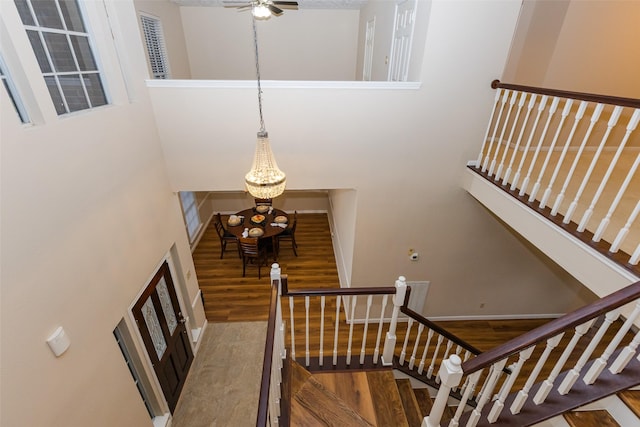 staircase featuring wood finished floors, a towering ceiling, a chandelier, a ceiling fan, and baseboards