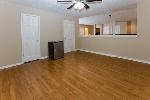 unfurnished room with ceiling fan, light wood finished floors, baseboards, and a textured ceiling
