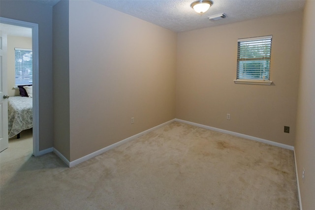 spare room featuring light carpet, plenty of natural light, baseboards, and a textured ceiling