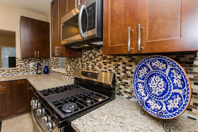 kitchen featuring stainless steel appliances, tasteful backsplash, light stone counters, and dark brown cabinetry