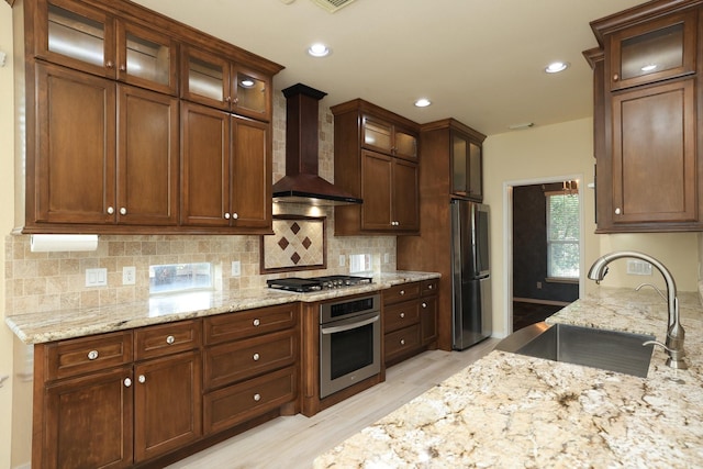 10606 Maidstone Manor Ct, Spring, TX 77379 - kitchen featuring appliances with stainless steel finishes, wall chimney range hood, a sink, light wood-style flooring, and light stone countertops