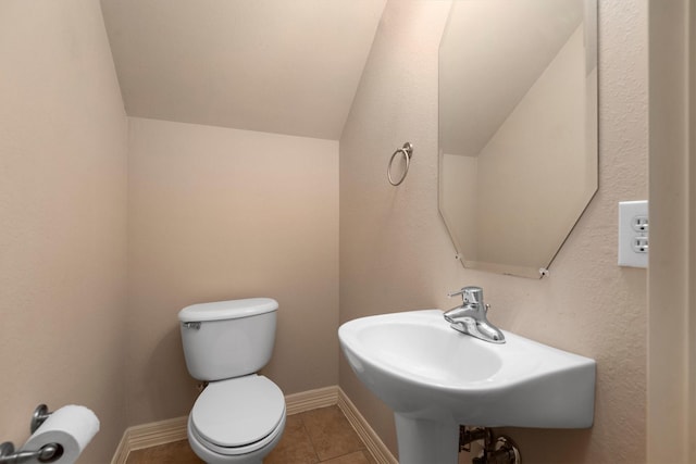bathroom with lofted ceiling, toilet, tile patterned floors, and a sink
