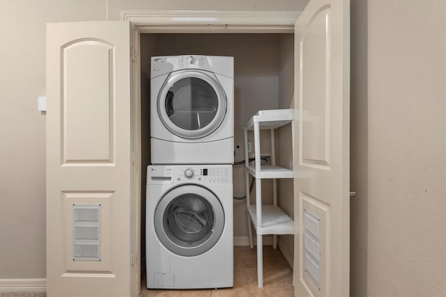 laundry area featuring stacked washer / drying machine, tile patterned flooring, and baseboards