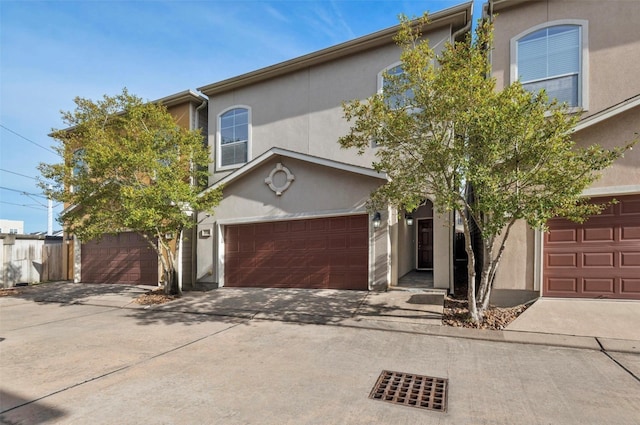 view of front of property featuring stucco siding, a garage, driveway, and fence