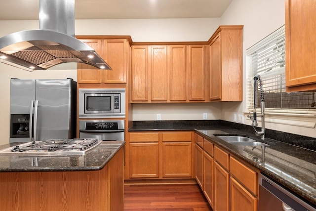 kitchen featuring appliances with stainless steel finishes, island range hood, dark wood-style flooring, a sink, and dark stone counters