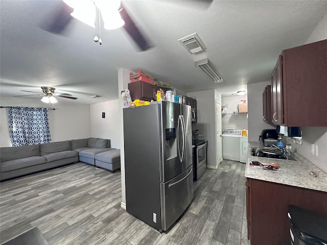 kitchen with appliances with stainless steel finishes, a ceiling fan, washer / dryer, wood finished floors, and a textured ceiling