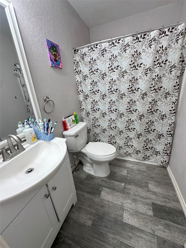 bathroom with toilet, wood finished floors, vanity, a textured wall, and curtained shower