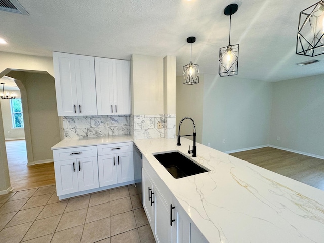 5318 Cilantro Ln, Baytown, TX 77521 - kitchen featuring a sink, decorative backsplash, arched walkways, white cabinets, and light stone counters