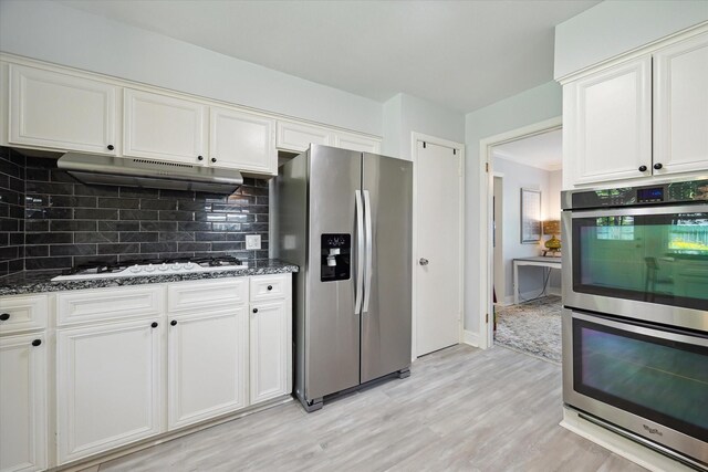 5402 Indigo St, Houston, TX 77096 - kitchen with appliances with stainless steel finishes, under cabinet range hood, decorative backsplash, light wood finished floors, and dark stone counters