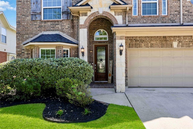 entrance to property featuring concrete driveway, brick siding, a garage, and stone siding