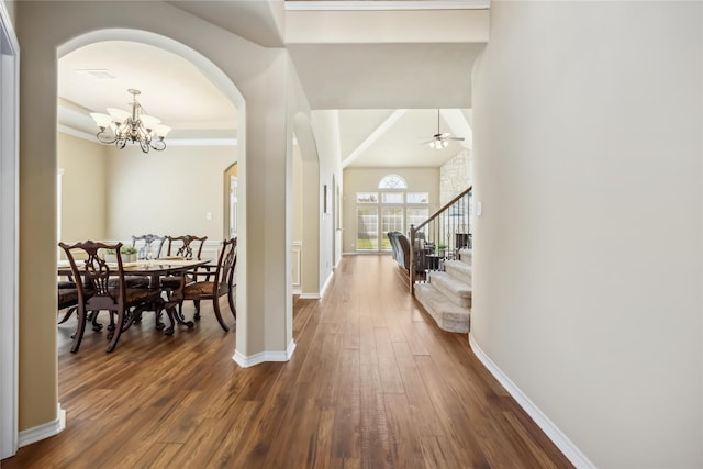 entrance foyer with arched walkways, dark wood-type flooring, a chandelier, stairs, and baseboards